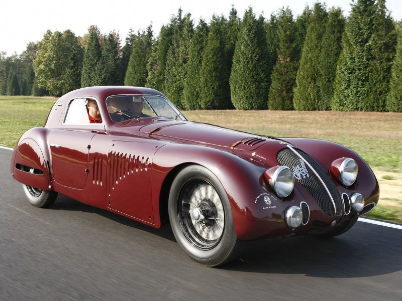 1938 red Alfa Romeo 8C 2900 Speciale Tipo Le Mans driving on a road with a line of trees in the background